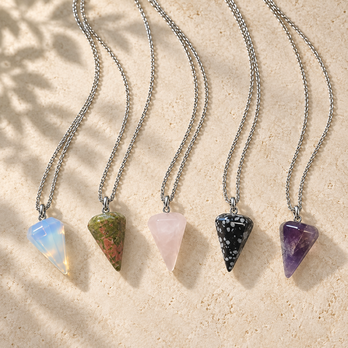 Five crystal pendulum necklaces arranged on a warm stone background