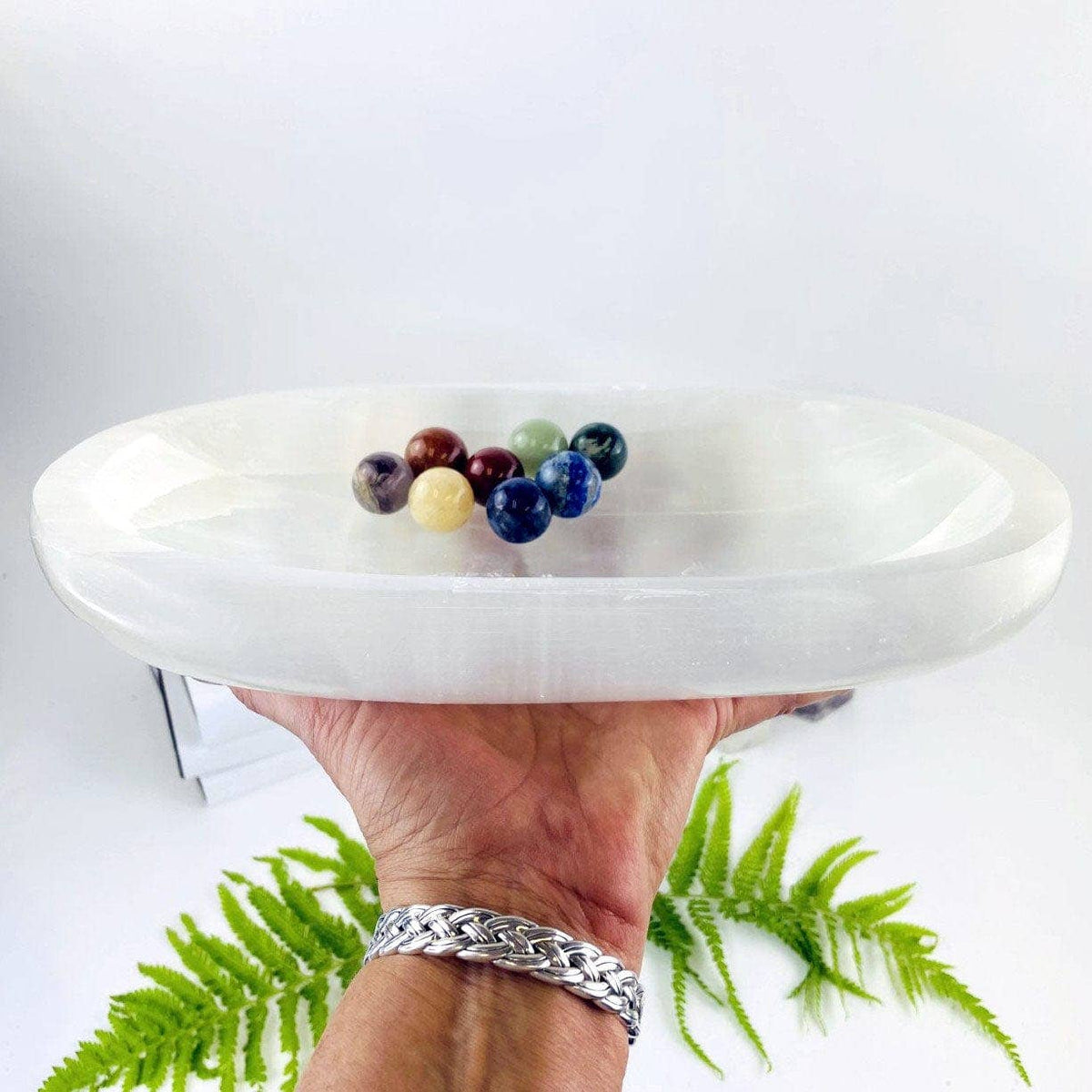 Extra large oval selenite bowl shown held in a hand with decorative stones